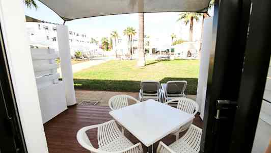 En uteplats med bord och stolar, och vy mot grönområde med solstolar. (AI-genererad text)