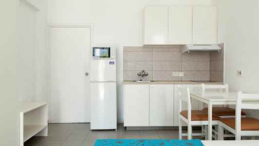 Ett kök med vit inredning, inklusive kylskåp, mikrovågsugn, och matbord med stolar. (AI-genererad text)