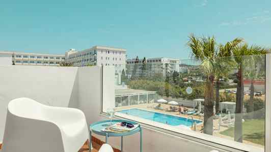 En terrass med vita stolar och ett bord, utsikt över en pool och omgivande byggnader. (AI-genererad text)