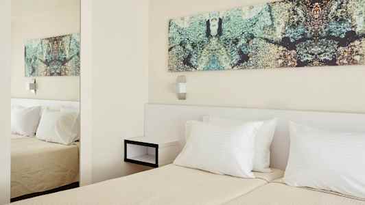 Ett ljust hotellrum med två enkelsängar. På väggen över sängarna hänger en stor väggdekor med mönster. Rummet har en modern och minimalistisk stil. (AI-genererad text)