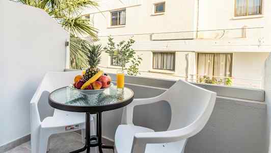 En balkong med ett bord som har en skål med frukt och ett glas med juice, omgiven av två vita stolar. (AI-genererad text)