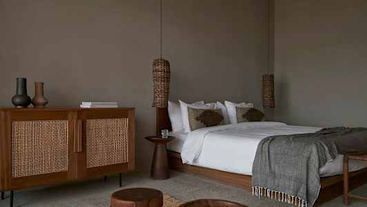 Ett sovrum med en stor säng, träbord och en skänk i rottingstil. (AI-genererad text)