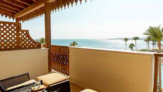 Balkong med korgmöbler och utsikt över havet samt palmer. (AI-genererad text)