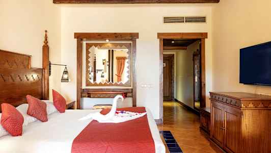 Ett hotellrum med en dubbelsäng som har röda kuddar och en dekoration formad som en svan på sängen. (AI-genererad text)