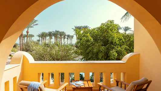 Balkong med sittmöbler framför en utsikt av träd och palmer. (AI-genererad text)