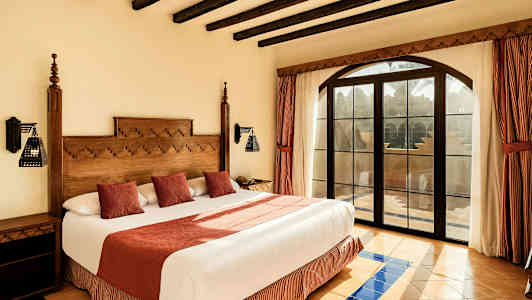 Ett rum med en stor säng, trädetaljer, röda gardiner och ett fönster med utsikt. (AI-genererad text)