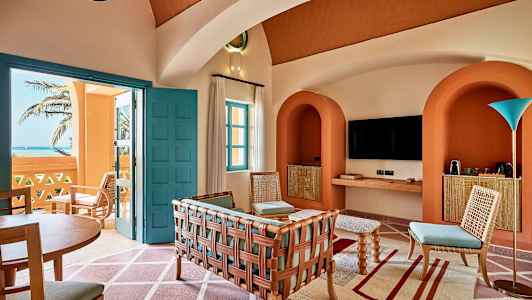 En inbjudande vardagsrumsinteriör med färgglada möbler, arkitektoniska bågar och utsikt mot havet genom en öppen dörr. (AI-genererad text)