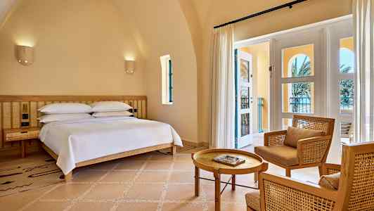 Ett rum med en säng, två stolar och ett bord, samt en glasdörr som leder ut till en balkong. (AI-genererad text)