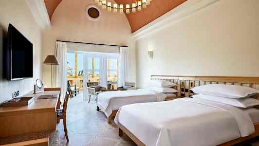 Hotellrum med två enkelsängar, skrivbord och sittgrupp vid balkongen. (AI-genererad text)