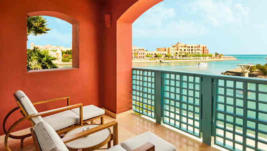 Utsikt från en balkong med sittmöbler, över en kustlinje och byggnader. (AI-genererad text)