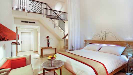 Modernt inredd hotellsvit med dubbelsäng, sittgrupp och trappa till loft. (AI-genererad text)