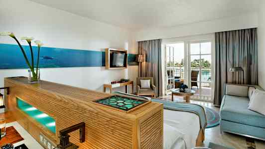 Inredning av ett ljust hotellrum med sittgrupp och balkong. (AI-genererad text)