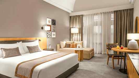 Bild av ett hotellrum med en stor säng, en soffa och ett bord framför gardiner. (AI-genererad text)