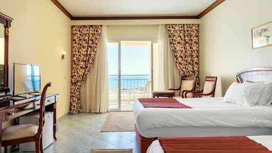 Hotelrum med vita väggar, två enkelsängar och en balkong med utsikt mot havet. (AI-genererad text)