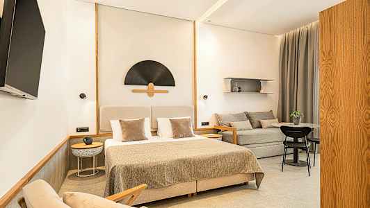 Ett stilrent hotellrum med en dubbelsäng, soffa, bord och en väggmonterad TV. (AI-genererad text)