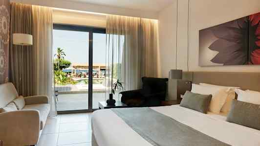 Hotellrum med dubbelsäng och utsikt över utomhusområdet genom en glasdörr. (AI-genererad text)