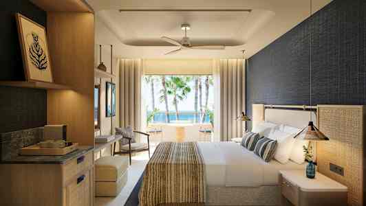 Ett hotellrum med ljus interiör och utsikt över palmer och hav. (AI-genererad text)