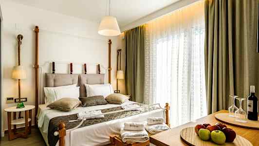 Ett hotellrum med en dubbelsäng, sängkläder och prydnadskuddar. Två handdukar och ett vinset är placerade på bänkar vid sängens fot. (AI-genererad text)