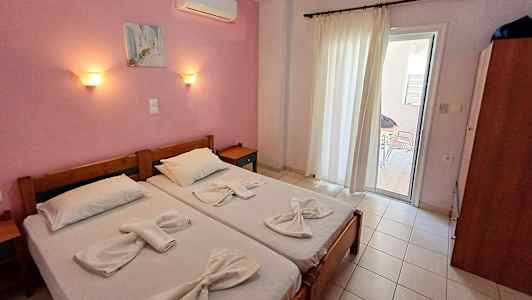 Två enkelsängar med vita sängkläder i ett rum med rosa väggar och ett glasdörr som leder ut till en balkong. (AI-genererad text)