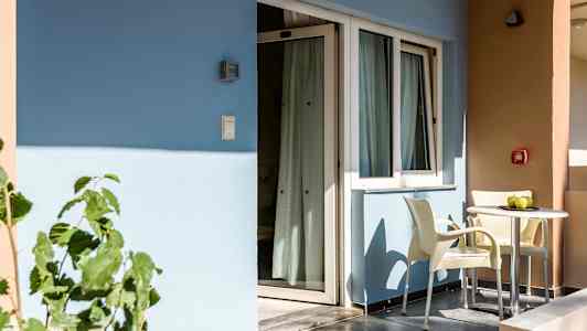 En balkong med två stolar och ett bord står framför en byggnad med blå och beige väggar. (AI-genererad text)