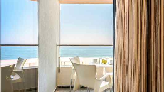 Balkongutsikt med bord och stolar samt havet i bakgrunden. (AI-genererad text)