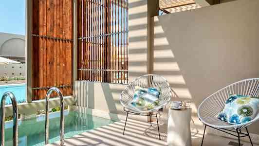 Två stolar med dynor står vid ett litet poolområde nära träpaneler. (AI-genererad text)