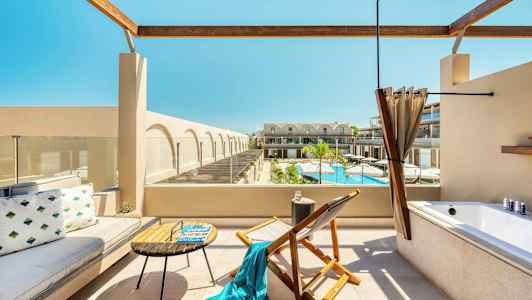 Terrass med sittmöbler, ett badkar och utsikt över en pool samt byggnader. (AI-genererad text)