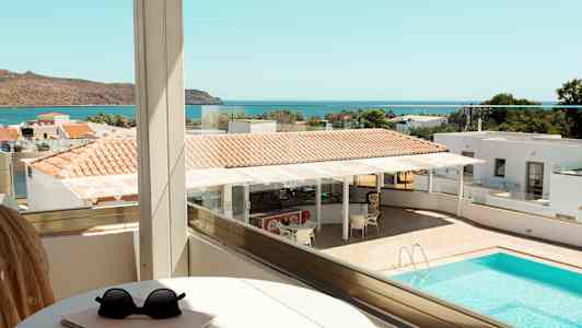 Utsikt från en balkong över en pool, delar av ett hotellområde och havet i bakgrunden. (AI-genererad text)