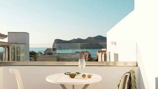 Utsikt från en terrass med ett bord, en stol och ett glas vin samt tilltugg, bakom syns havet och berg. (AI-genererad text)