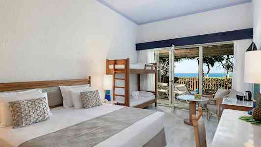 Hotellrum med dubbelsäng, våningssäng och utgång till altan med havsutsikt. (AI-genererad text)