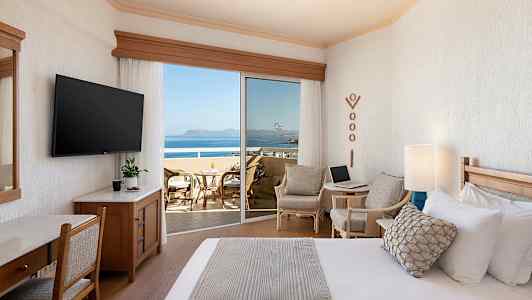 Ett hotellrum med en säng, sittgrupp och en balkong med utsikt över havet. (AI-genererad text)