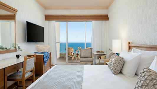 Hotellrum med utsikt mot havet genom stora glasdörrar. (AI-genererad text)