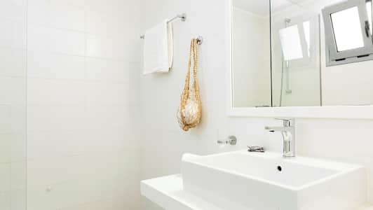 Ett ljust badrum med vit kakelvägg, tvättställ, handdukshängare och spegel. (AI-genererad text)