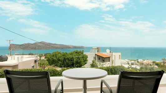 Två stolar och ett bord på en balkong med utsikt över havet och kustlandskapet. (AI-genererad text)