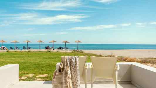 En strand med solstolar och parasoller med havet i bakgrunden, en uteplats med stolar i förgrunden. (AI-genererad text)