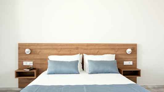 Säng med blå överkast och kuddar, träbord på vardera sidan. (AI-genererad text)