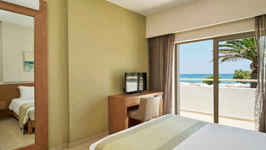 Hotellrum med säng, TV och skrivbord samt utsikt över havet genom ett fönster. (AI-genererad text)