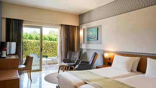 Hotellrum med två sängar, sittgrupp, fönster mot grönska. (AI-genererad text)