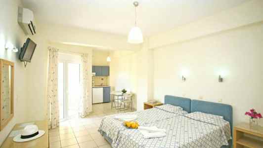 Ett ljust rum med två enkelsängar, ett kök i hörnet och en glasdörr som leder till balkongen. (AI-genererad text)