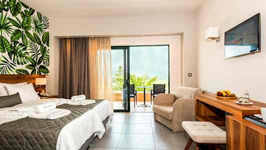 Ett hotellrum med dubbelsäng, sittgrupp, balkong och väggdesign med bladmotiv. (AI-genererad text)