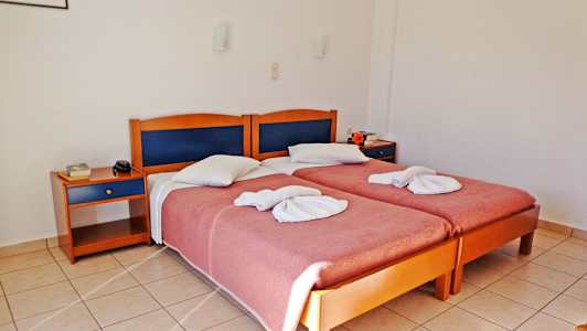 Två enkelsängar med höft handdukar och rosa överkast, två nattygsbord och en golvbeläggning av plattor i ett hotellrum. (AI-genererad text)