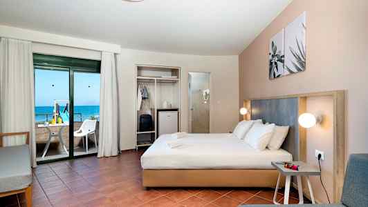 Hotellrum med dubbelsäng, sittgrupp och balkong med utsikt över havet. (AI-genererad text)