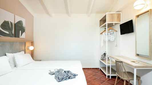 Ett hotellrum med en dubbelsäng, skrivbord, stol och öppet klädställ. (AI-genererad text)