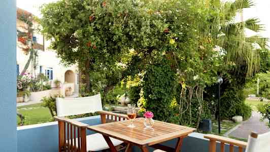 En terrass med två stolar, ett bord med en rosa blomma i en vas och ett glas dryck, omgiven av frodig grönska. (AI-genererad text)