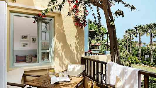 En balkong med trädgårdsutsikt, bord och stolar samt en vattenkaraff med glas. (AI-genererad text)