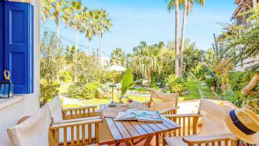 En terrass med trädgårdsmöbler, utsikt över en solig trädgård med palmer och grönska. (AI-genererad text)