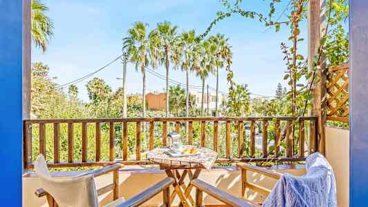 Balkong med två stolar, ett bord och utsikt över palmträd. (AI-genererad text)