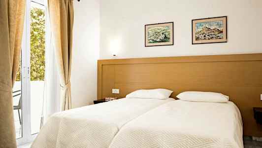 Ett sovrum med två enkelsängar, en träram, ljusa lakan, och två tavlor ovanför sängarna. (AI-genererad text)