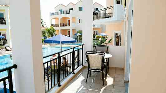 En balkong med möblemang, utsikt mot en pool och orange byggnader. (AI-genererad text)