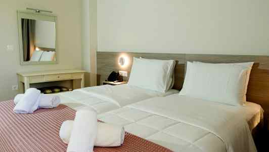 Två enkelsängar med vita sängkläder och rosa överkast, samt hoprullade vita handdukar ovanpå. (AI-genererad text)